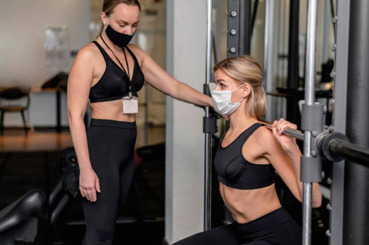 A woman in athletic wear performs a squat under the guidance of a trainer in a modern gym setting.