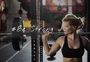 A woman lifts a heavy barbell in a gym, showcasing strength and determination, with a motivational hashtag overlayed.