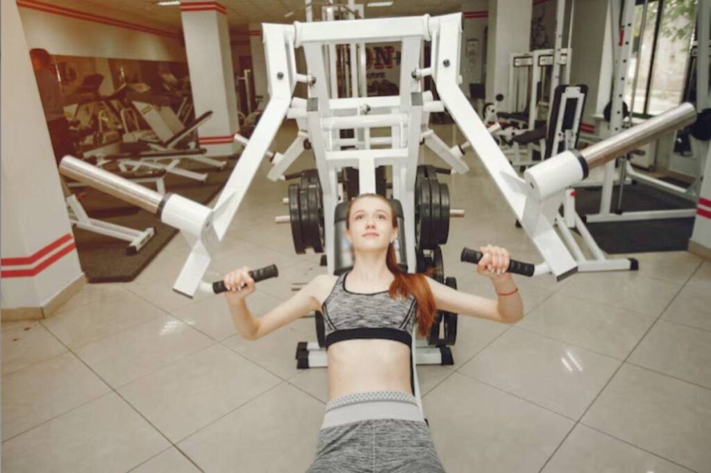 A person exercises on a weight lifting machine in a bright gym, surrounded by various fitness equipment and mirrors.