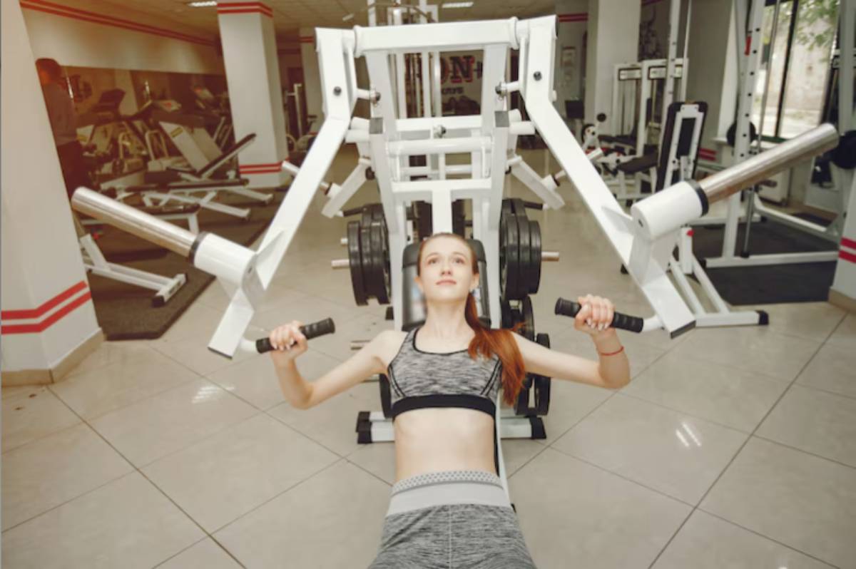 A person exercises on a weight lifting machine in a bright gym, surrounded by various fitness equipment and mirrors.