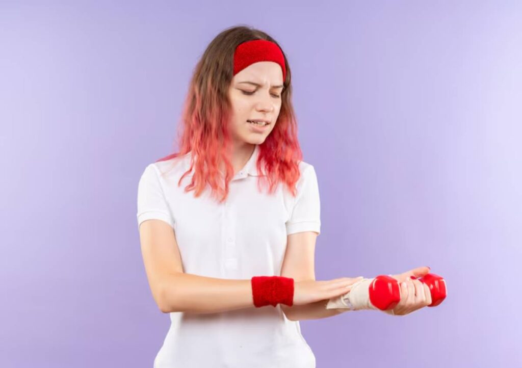 A person wearing a white shirt and red workout accessories holds red dumbbells against a lilac background.