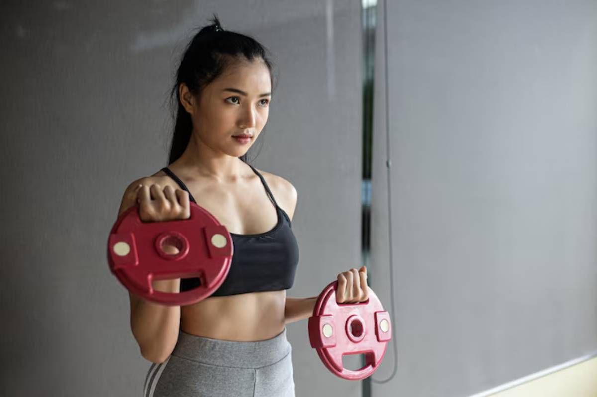 A person in athletic wear holds two red weight plates, showcasing strength and fitness in a gym setting.
