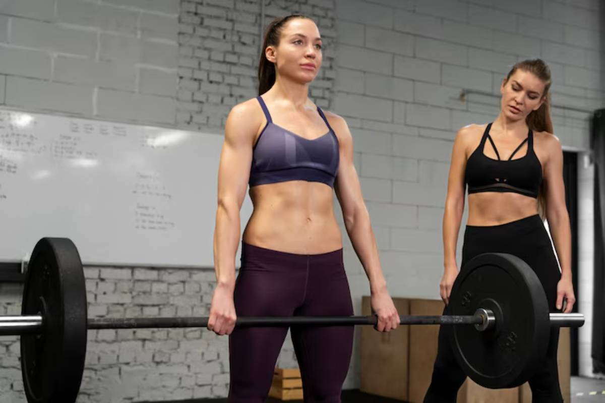 A fit individual is deadlifting a barbell in a gym, while another person observes attentively, showcasing a focused training environment.