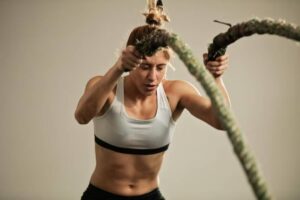 A fit individual exercises with thick battle ropes, showcasing strength and focus, against a neutral background.