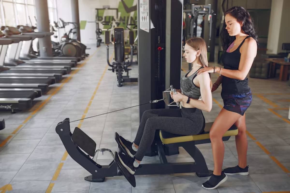 A woman demonstrates proper form while using a cable machine in a modern gym, with workout equipment in the background.