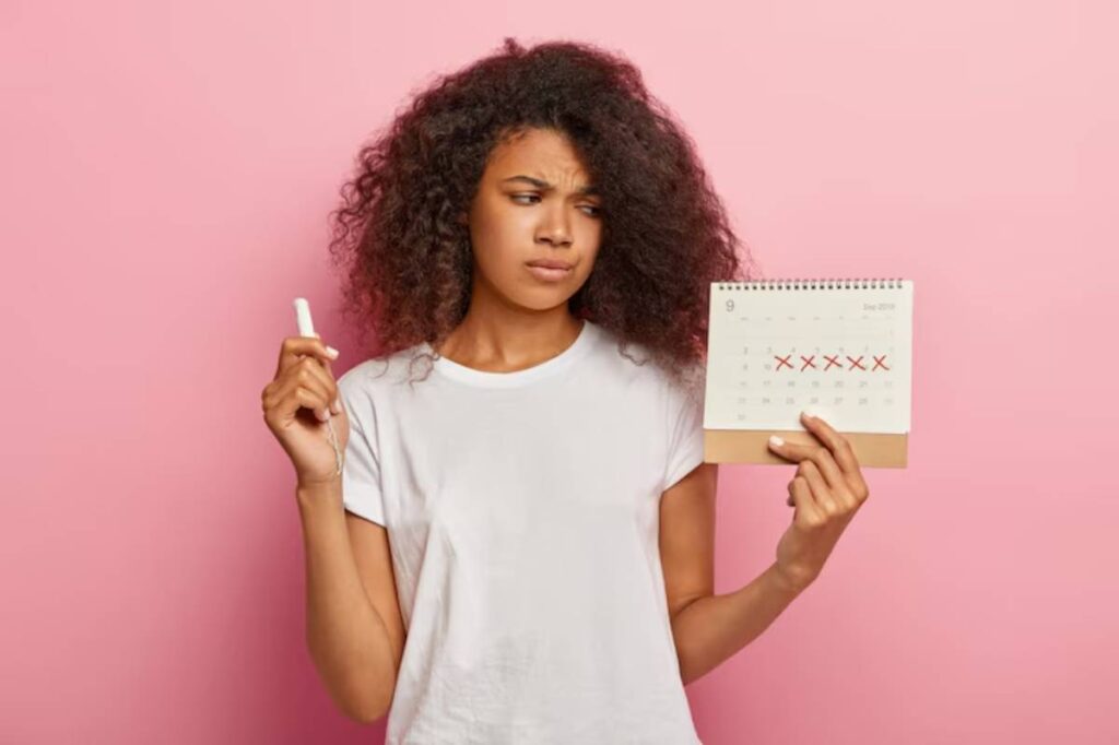 A person holds a calendar marked with red Xs on specific dates, while also holding a white marker against a pink background.