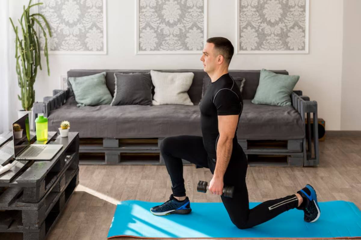  A person performs a lunge with dumbbells on a yoga mat in a cozy living room with green plants and a laptop on a wooden table.