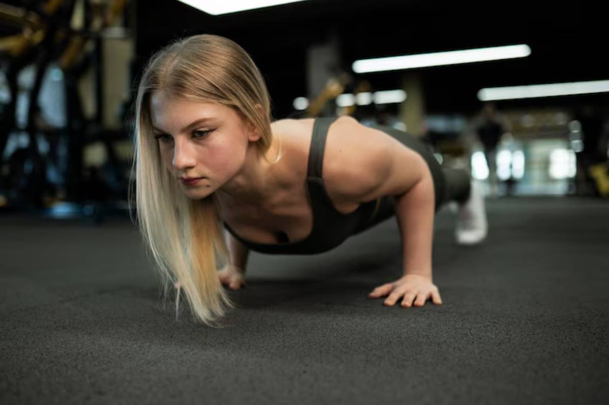 A person performs a push-up on a black gym floor, showcasing strength and focus in a well-lit fitness environment.