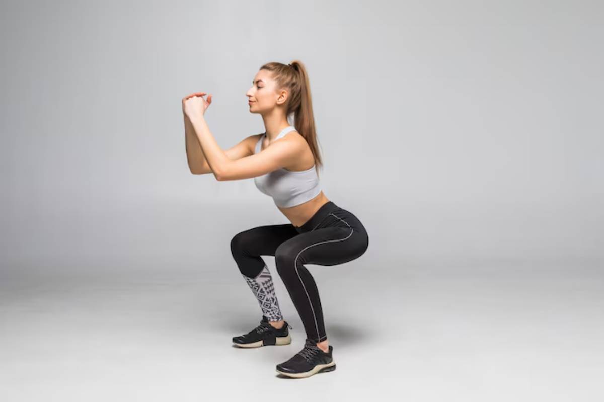 A person in athletic wear performs a squat in a minimalistic studio setting, showcasing focused fitness engagement.