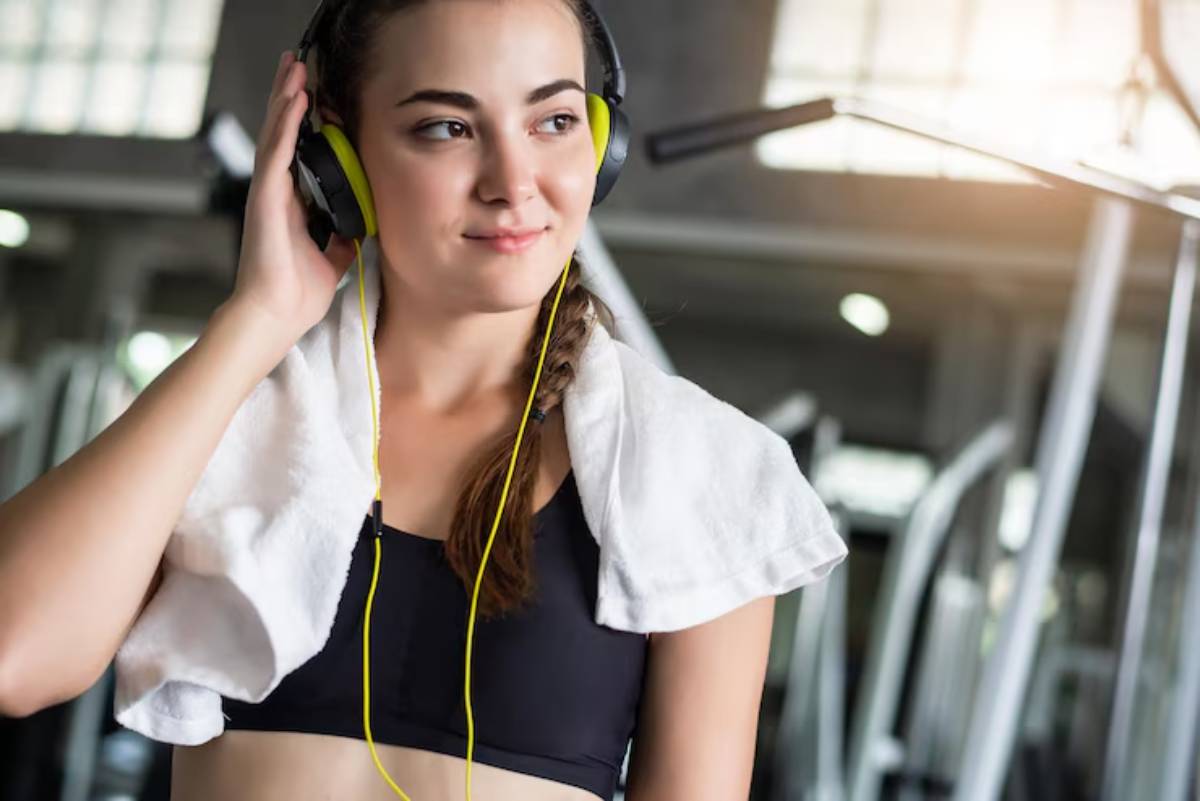 A person in a workout outfit wearing yellow headphones, with a towel draped around their neck, in a gym setting.