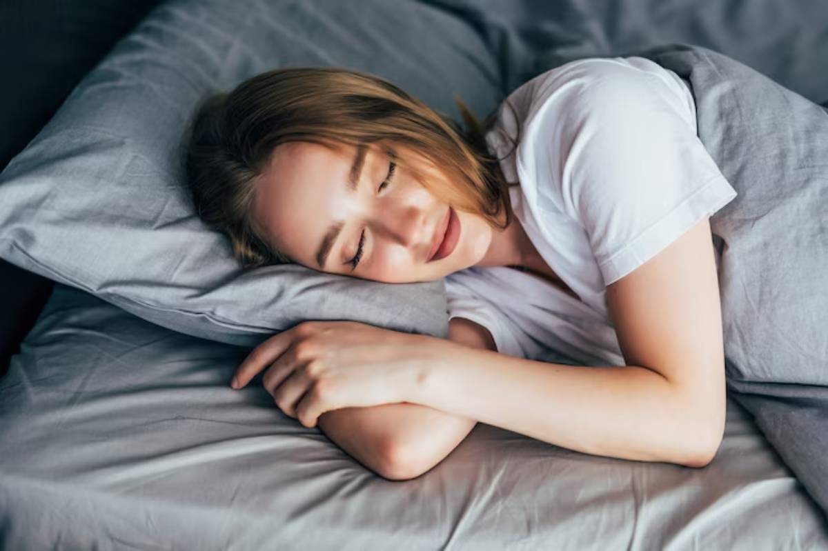 A person in a white shirt is resting on gray pillows, peacefully lying on a bed, showcasing a serene and relaxed atmosphere.